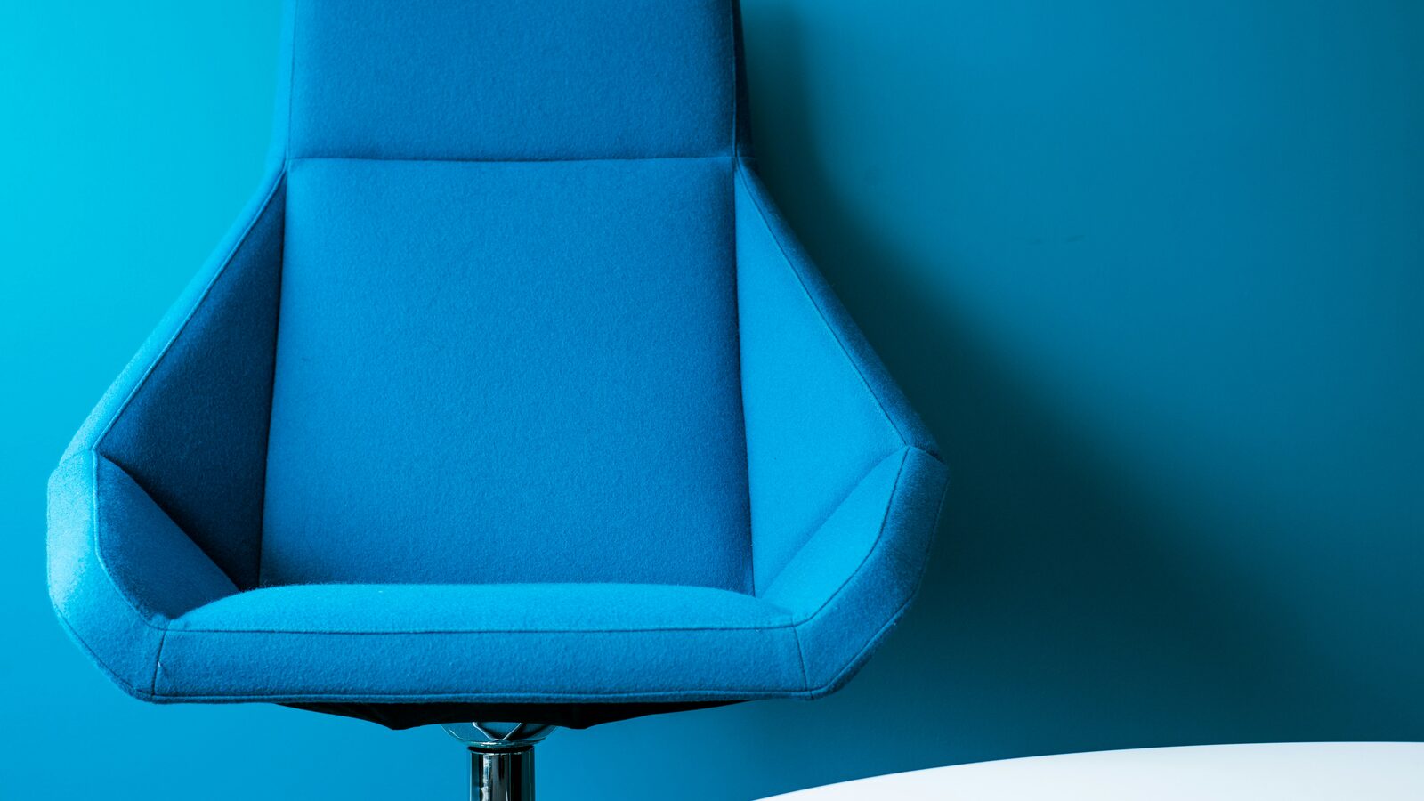 A single blue padded swivel chair standing against a bare wall