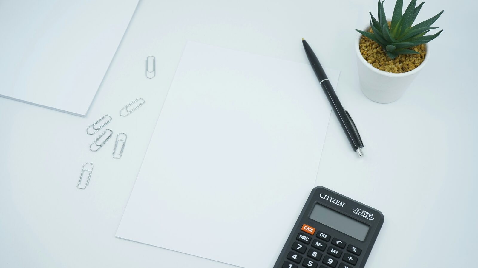 A black calculator and a pen resting on a blank sheet of paper