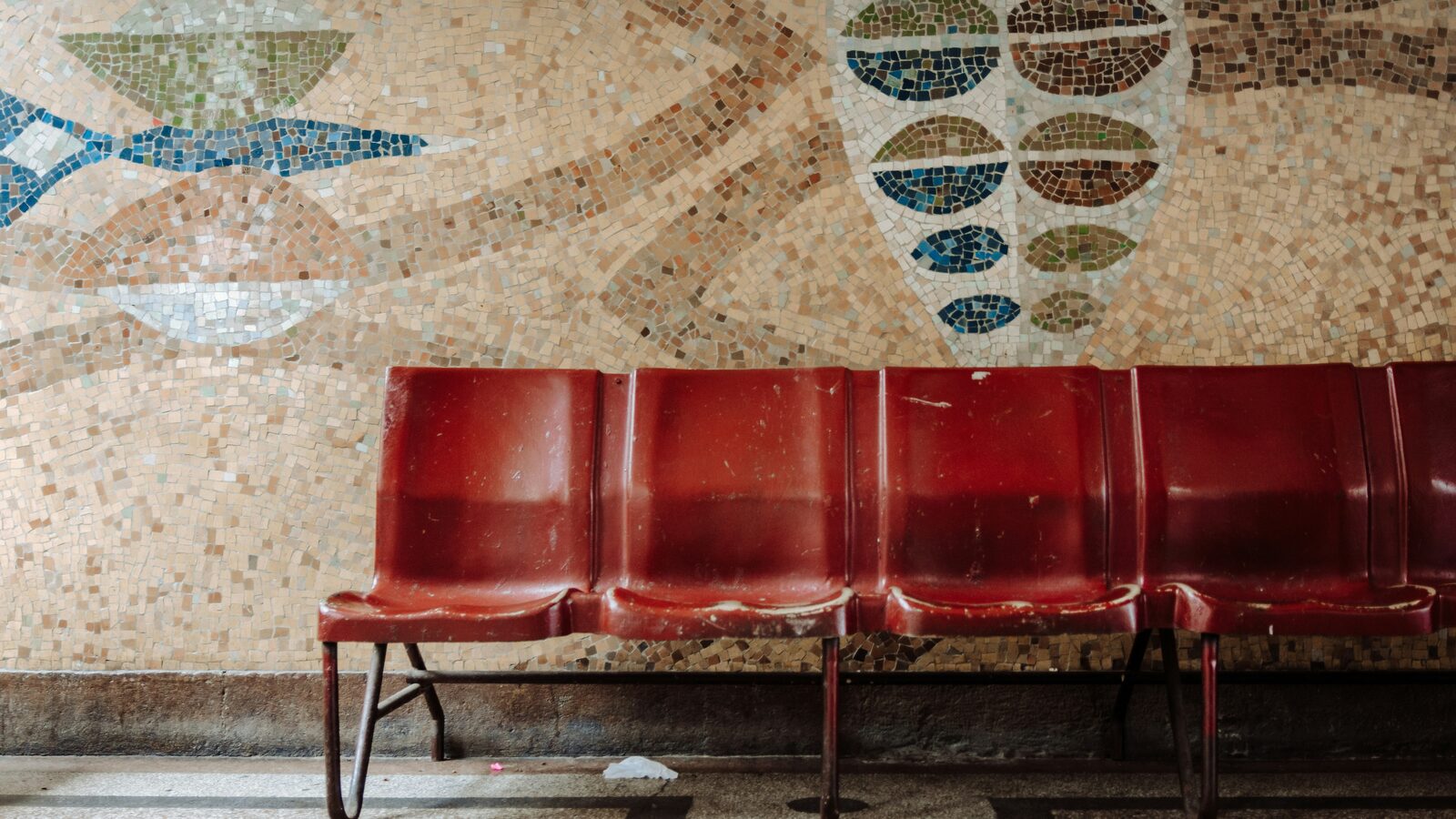 Five red chairs in a row against a pale wall